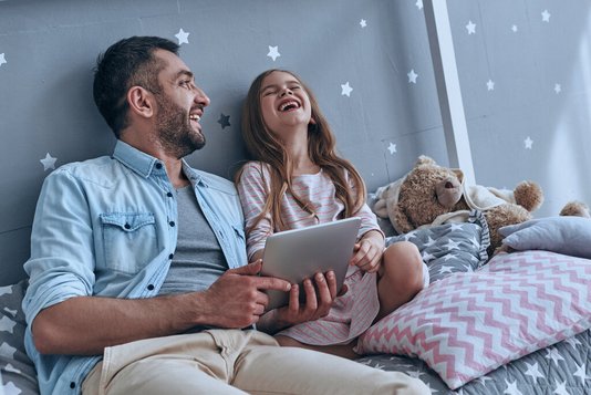 Vater und Tochter schauen auf ein Tablet und lachen 